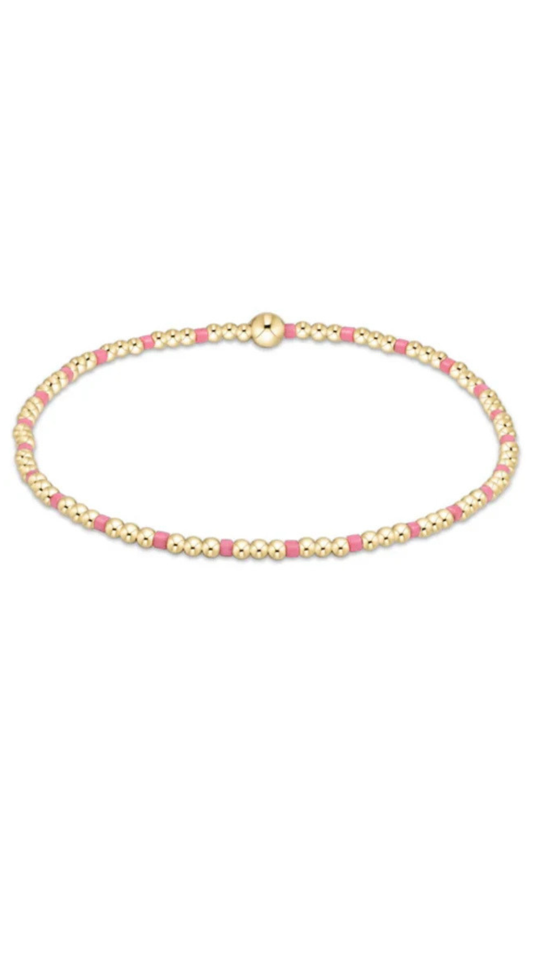 A delicate beaded bracelet featuring alternating rows of small gold-toned beads and pink beads, with a polished gold clasp, shown on a plain white background.