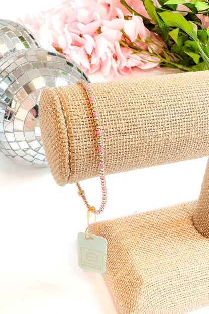 Pink beaded bracelet on a burlap roll with flowers and disco ball in the background