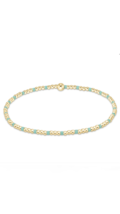 A delicate beaded bracelet featuring alternating light blue-green beads and textured gold beads, with a matching gold clasp, shown on a plain white background.