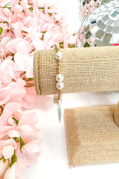 beaded bracelet with pearl detailing on a white surface with pink flowers in the background