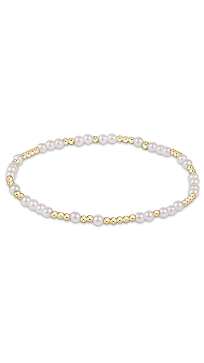 A delicate beaded bracelet featuring white pearls and small polished gold beads, arranged in a horizontal oval on a solid white background.