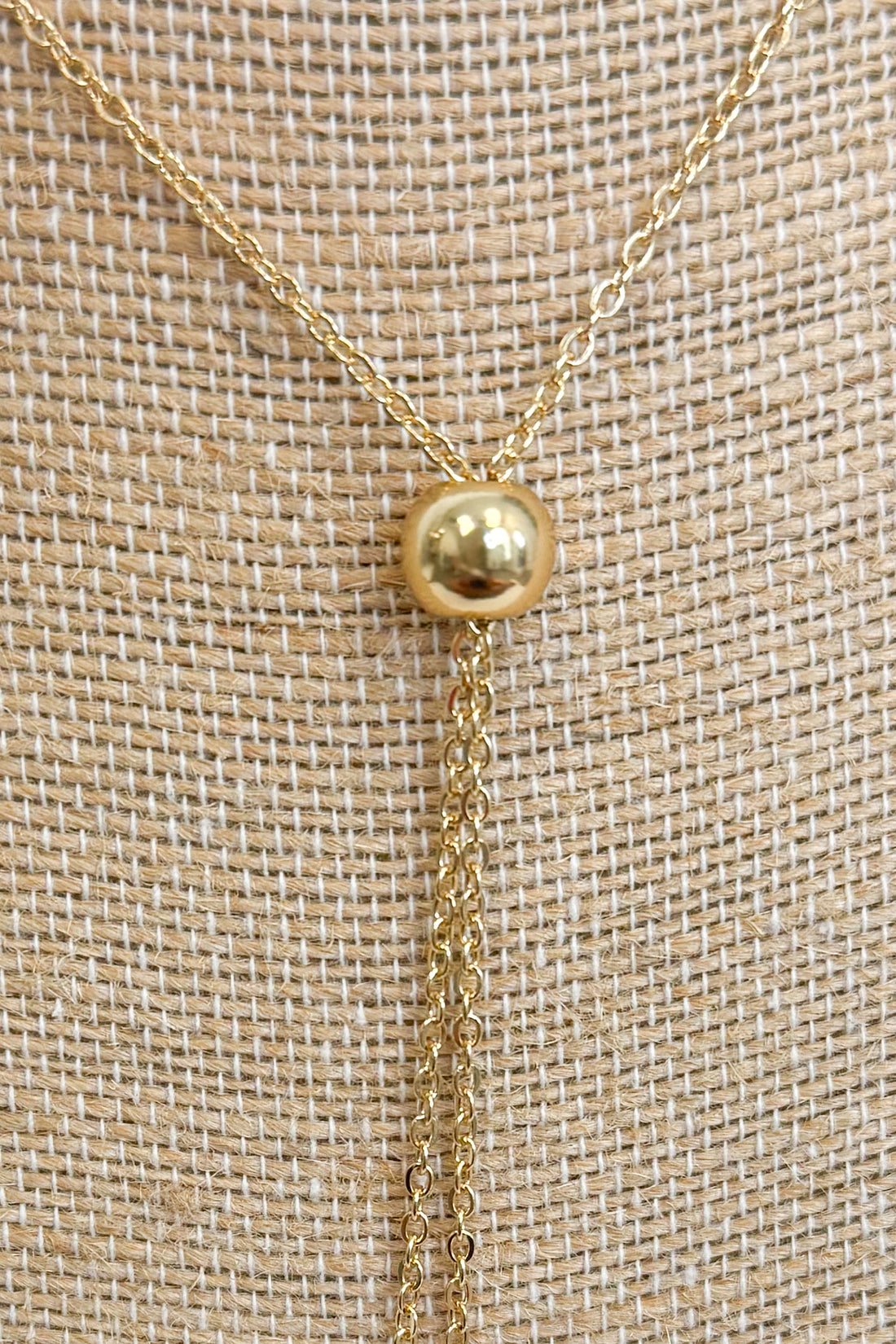 Close up of gold-tone bolo necklace featuring a fine, reflective chain held together by a smooth, polished gold sphere slider