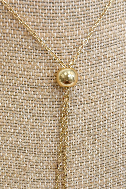 Close up of gold-tone bolo necklace featuring a fine, reflective chain held together by a smooth, polished gold sphere slider