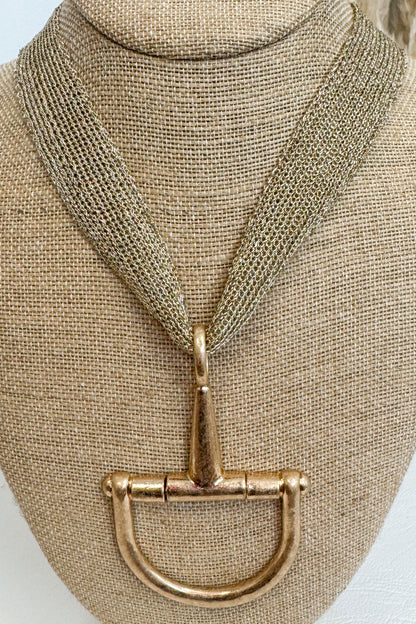 Gold-tone mesh necklace featuring a large horsebit pendant, displayed on a beige jewelry bust against a white studio background