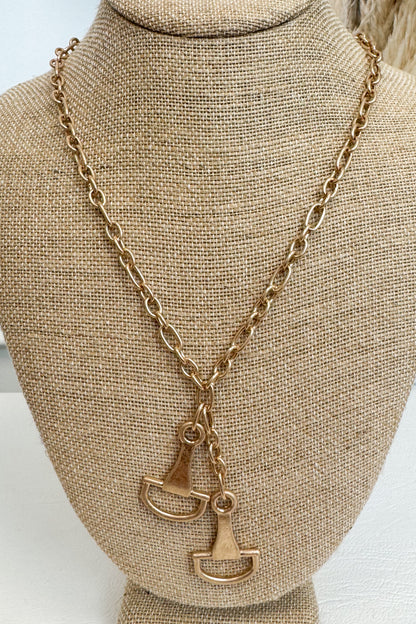 Gold-tone delicate chain necklace featuring two horsebit pendants, shown on a beige jewelry bust