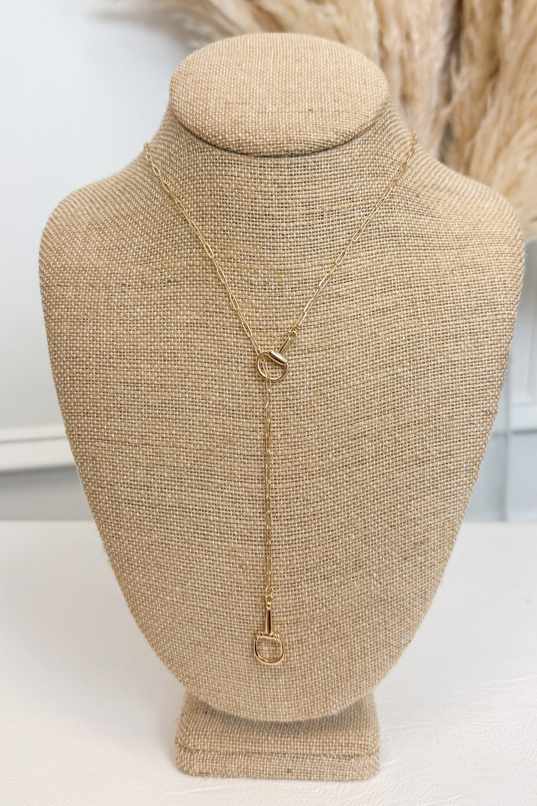 Gold-tone delicate chain necklace featuring a small horsebit pendant, displayed on a beige jewelry bust against a white studio background