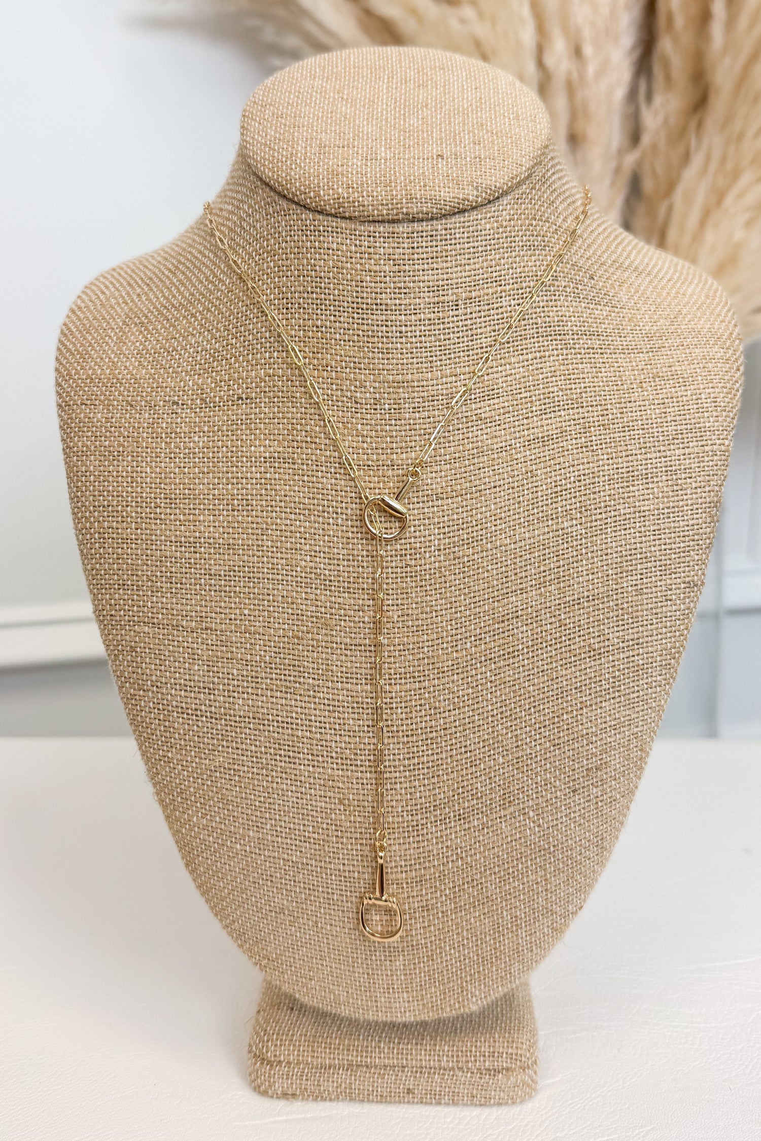 Gold-tone delicate chain necklace featuring a small horsebit pendant, displayed on a beige jewelry bust against a white studio background