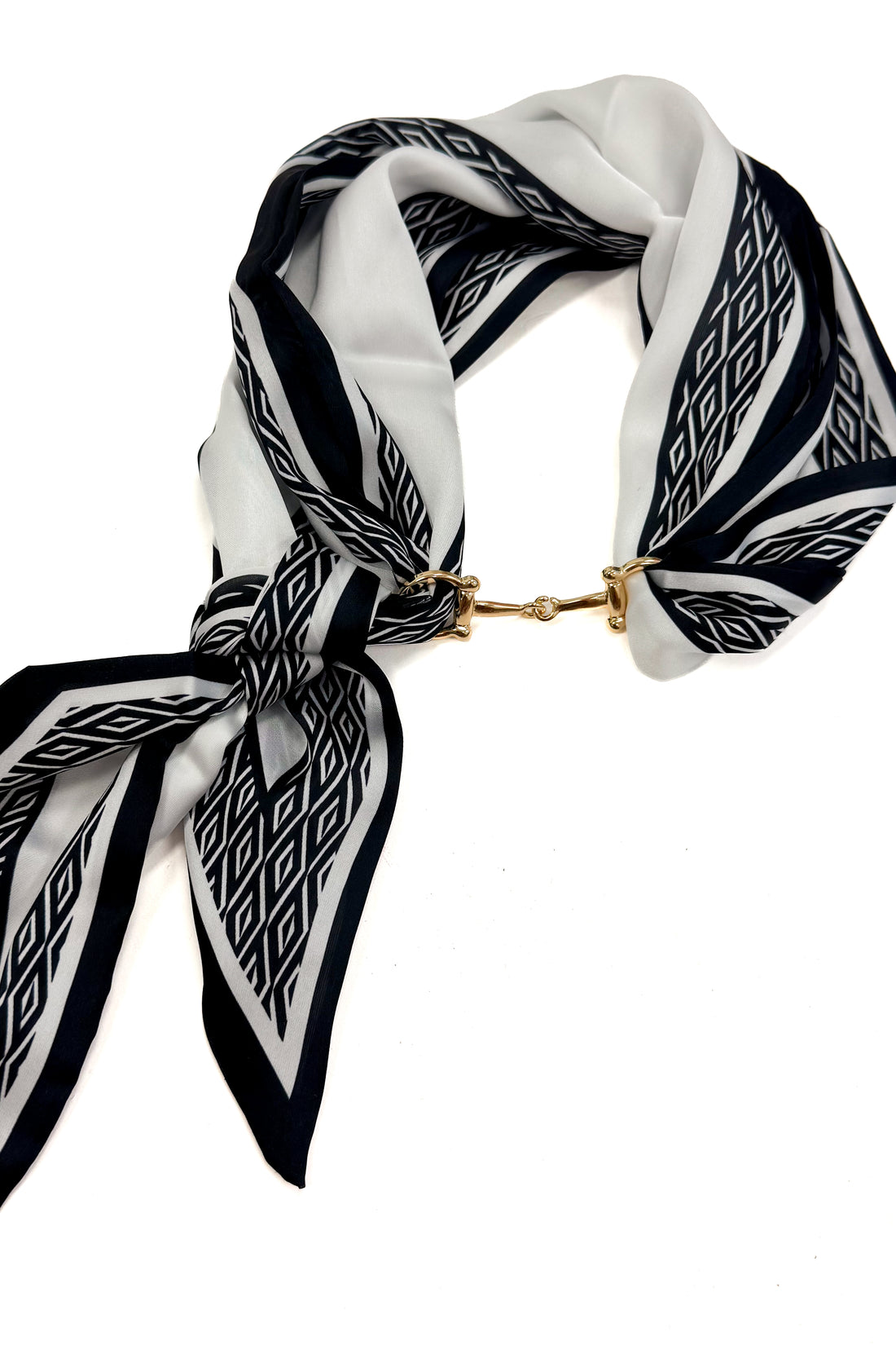 A black and white patterned silk scarf with a gold horsebit clasp, styled in a knot on a plain white background.