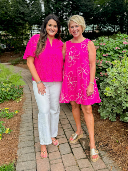 Front view of woman wearing Swagger Boutique’s Hot Pink Flutter Sleeve Eyelet Top with jeans and woman wearing a hot pink dress walking down a path outside.