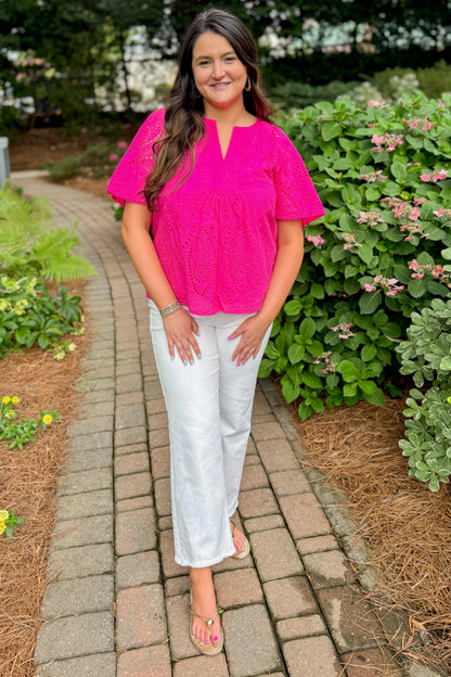 Front view of woman wearing Swagger Boutique’s Hot Pink Flutter Sleeve Eyelet Top with jeans walking down a path outside.