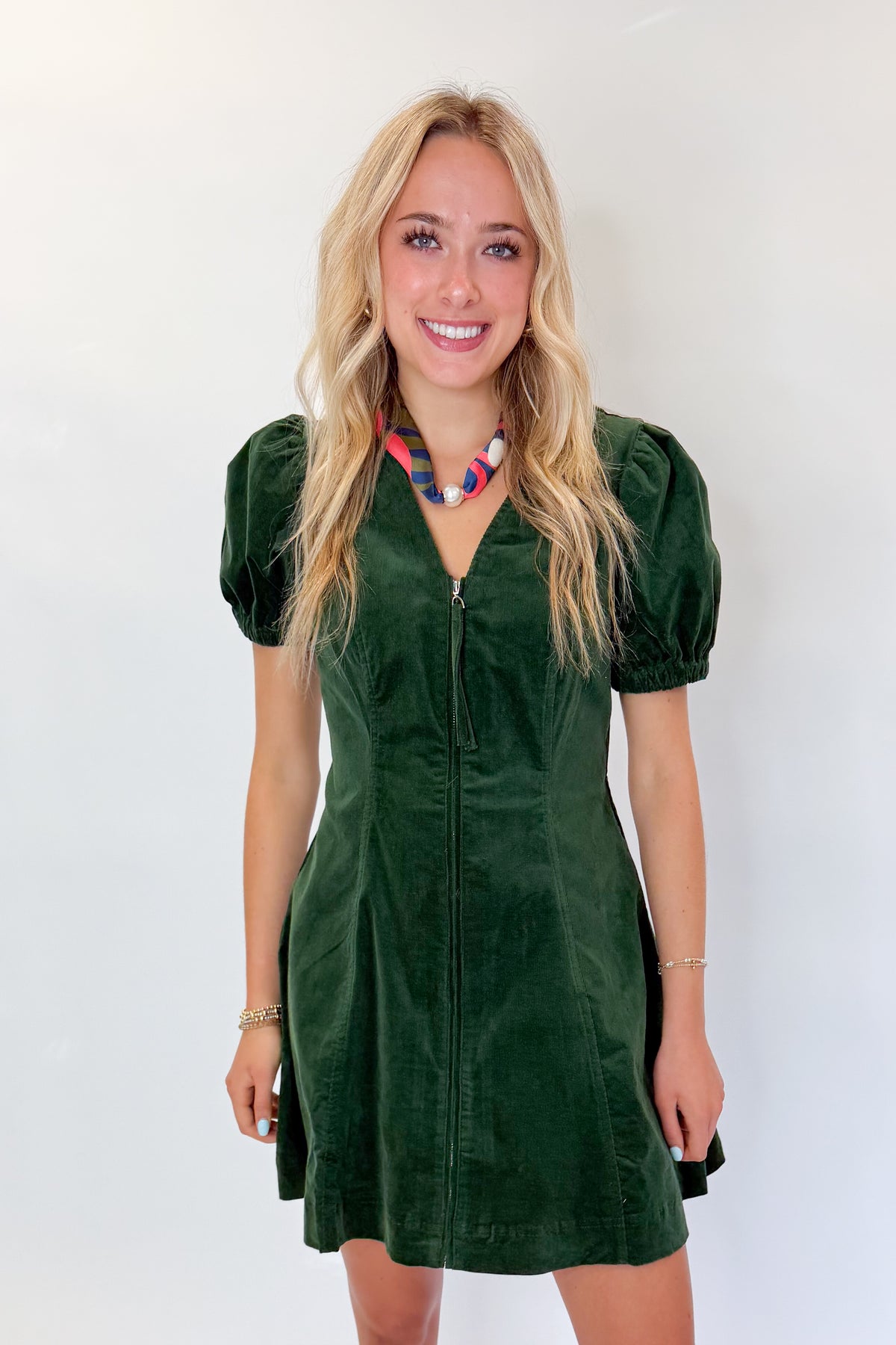 Front view of woman wearing Swagger Boutique’s Hunter Green Corduroy Mini Dress by Entro with boots against white studio background.