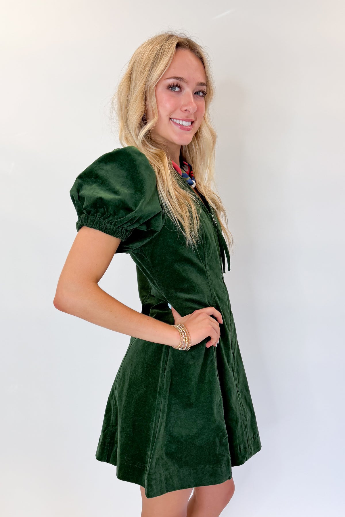 Side view of woman wearing Swagger Boutique’s Hunter Green Corduroy Mini Dress by Entro with boots against white studio background.