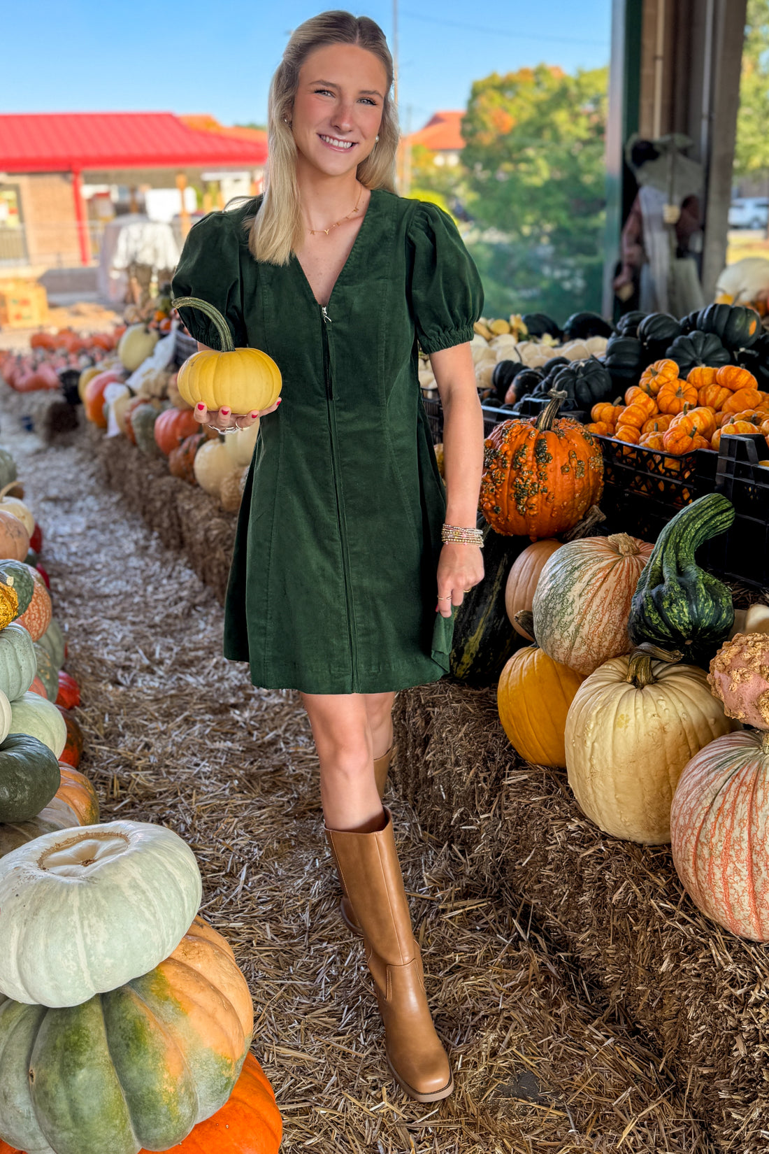 Front view of woman wearing Swagger Boutique’s Hunter Green Corduroy Mini Dress by Entro with boots at a pumpkin patch.