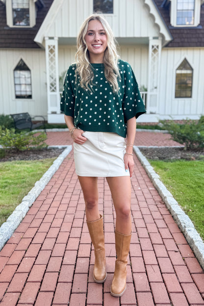 Front detail view of woman wearing Swagger Boutique’s Hunter Green Polka Dot Short Sleeve Sweater by Entro with skirt standing in front of a white house.