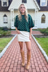 Front detail view of woman wearing Swagger Boutique’s Hunter Green Polka Dot Short Sleeve Sweater by Entro with skirt standing in front of a white house.