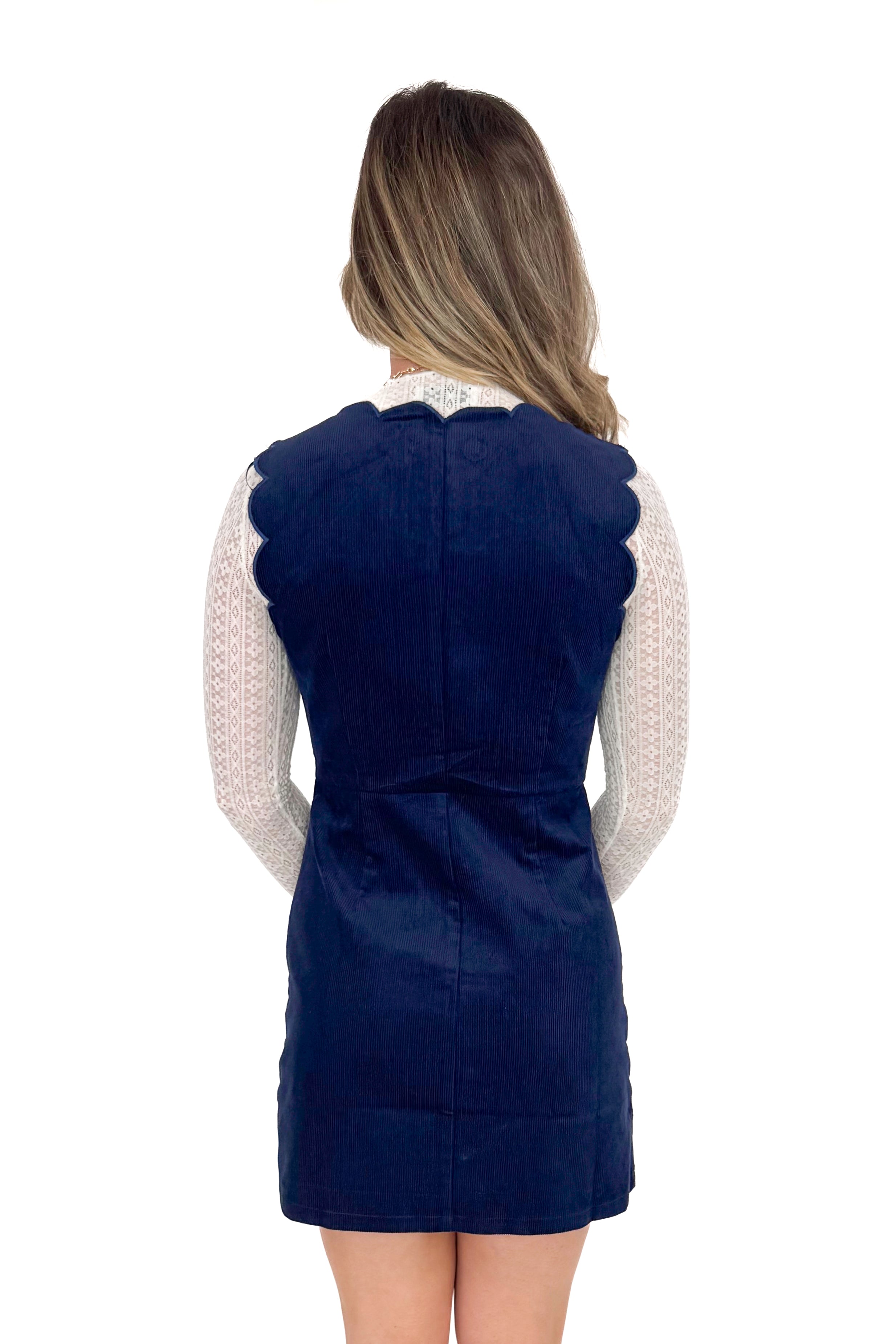 Back view of model wearing Navy Corduroy Scallop Lined Dress with boots against white studio background.