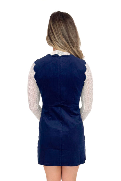 Back view of model wearing Navy Corduroy Scallop Lined Dress with boots against white studio background.