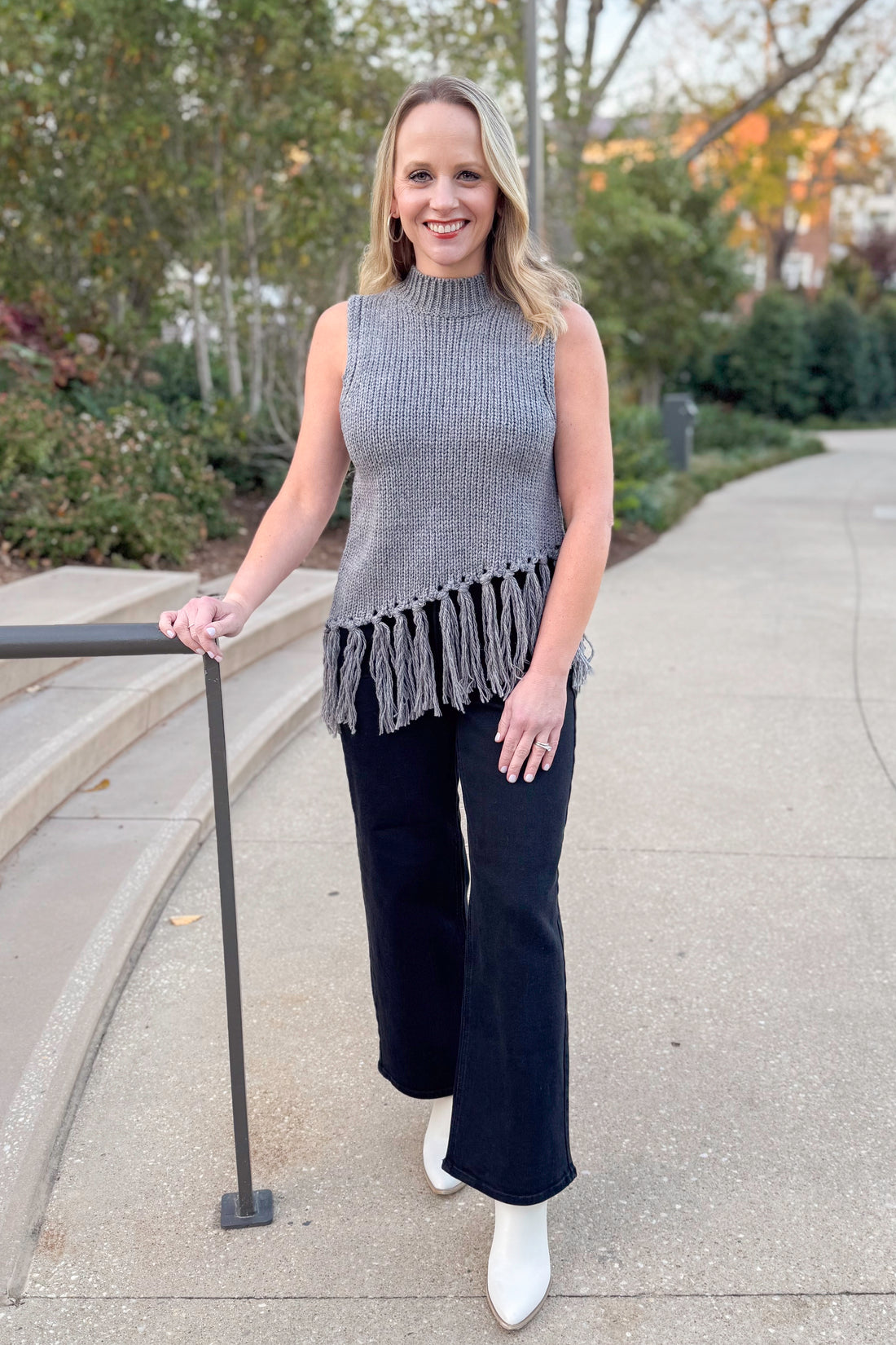 Front view of woman wearing Grey Mock Neck Fringe Detail Sleeveless Sweater and jeans outside.