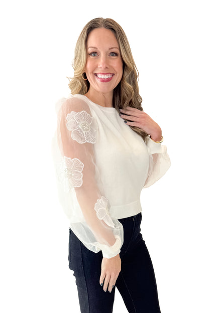 Side view of woman wearing Off White Floral Applique Sleeve Sweater with jeans against white studio background.