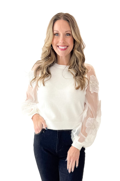 Front view of woman wearing Off White Floral Applique Sleeve Sweater with jeans against white studio background.