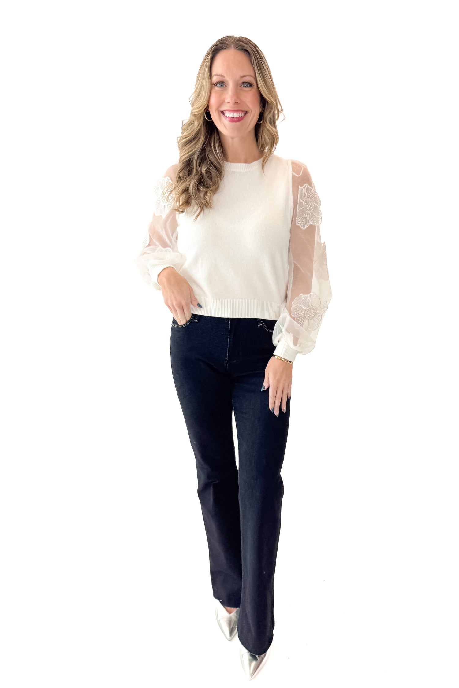 Front view of woman wearing Off White Floral Applique Sleeve Sweater with jeans against white studio background.