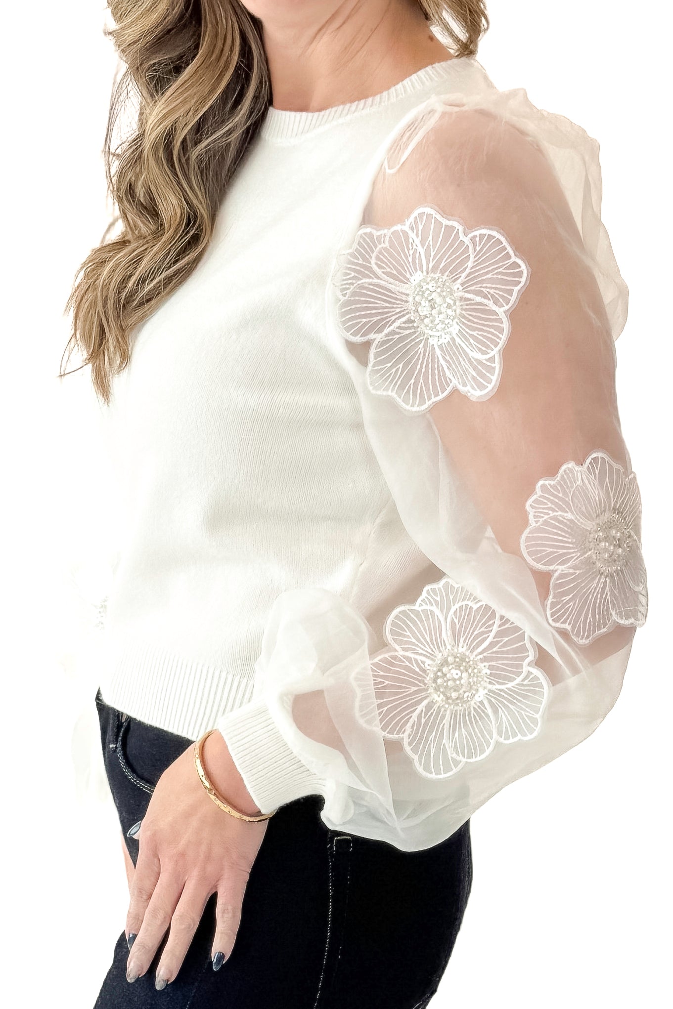 Side detail view of woman wearing Off White Floral Applique Sleeve Sweater with jeans against white studio background.