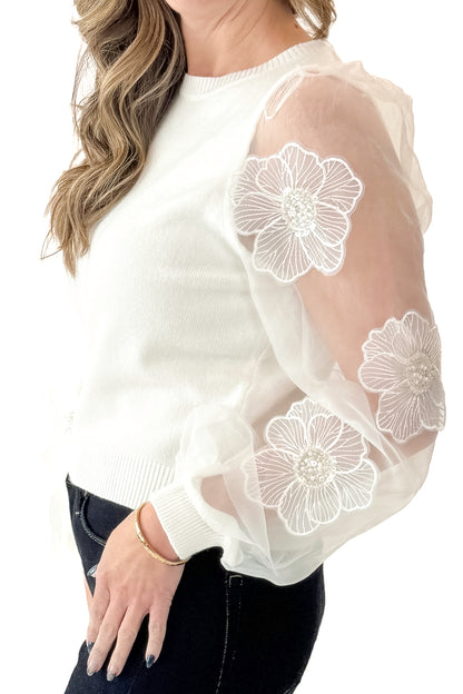 Side detail view of woman wearing Off White Floral Applique Sleeve Sweater with jeans against white studio background.