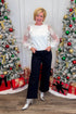 Front view of woman wearing Off White Floral Applique Sleeve Sweater with jeans around holiday decor.
