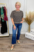 Woman in a patterned top and blue jeans standing in a room with a clothing rack and decorative elements.