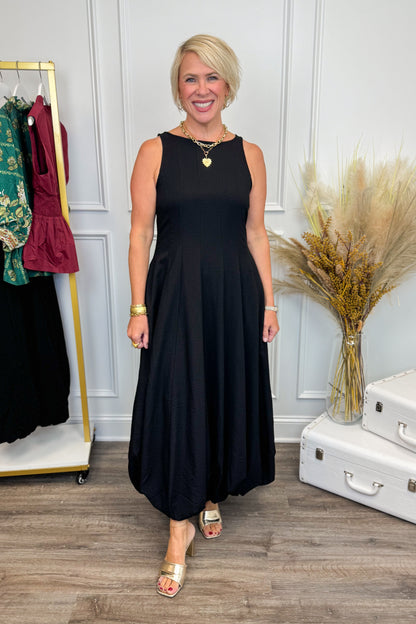 Woman wearing Black Bubble Hem Midi Dress with clothes in the background.