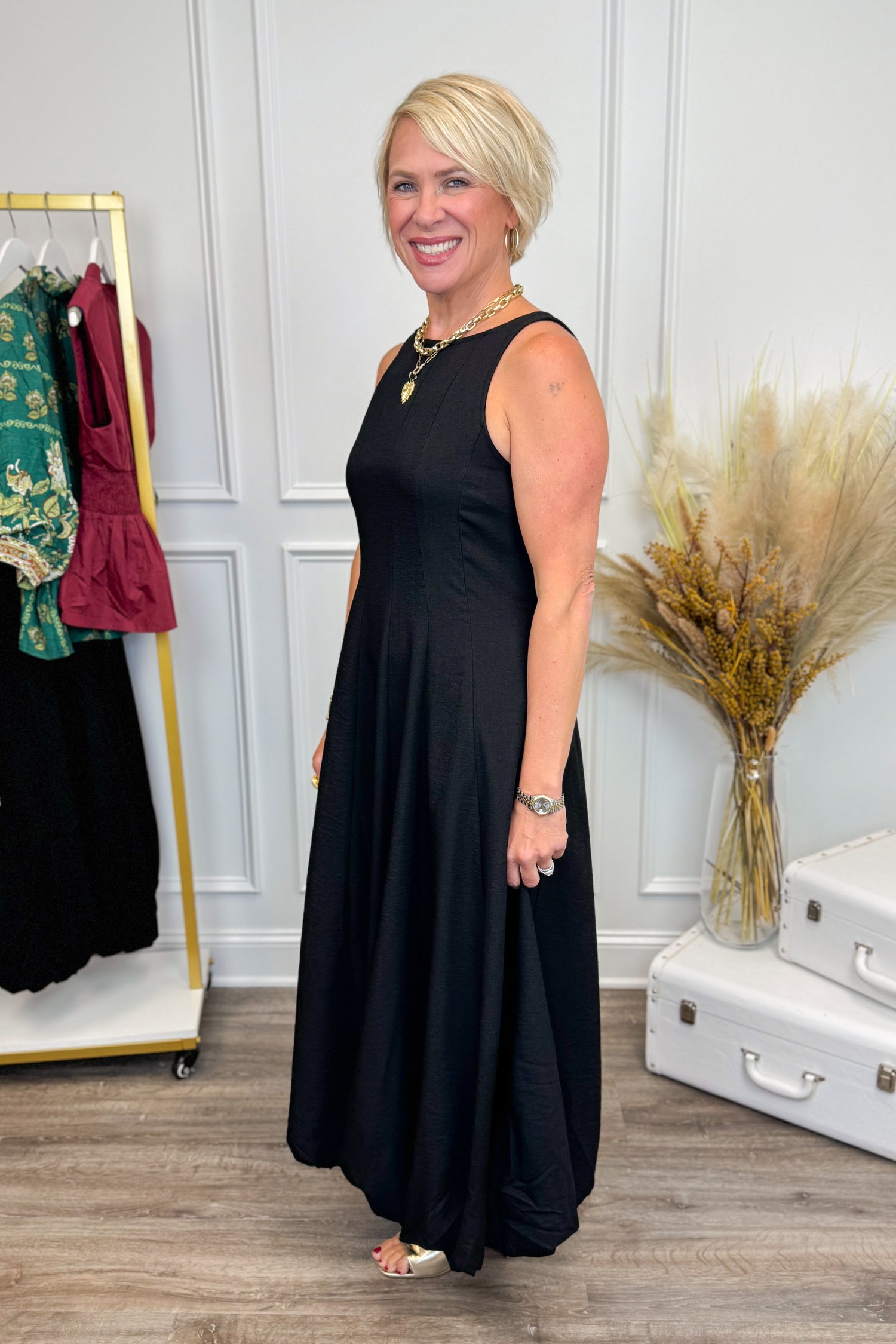 Side view of Woman wearing Black Bubble Hem Midi Dress with clothes in the background.