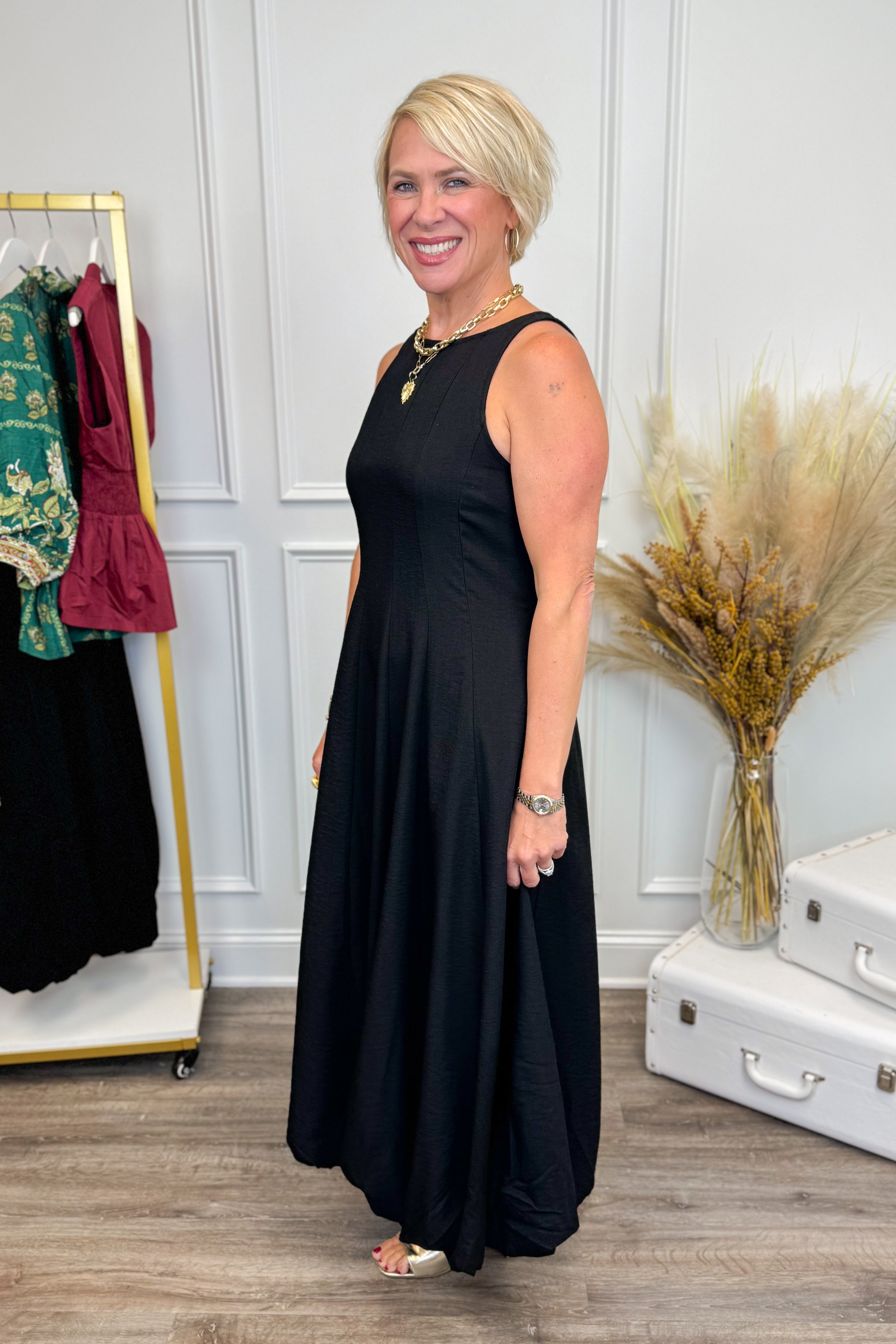 Side view of Woman wearing Black Bubble Hem Midi Dress with clothes in the background.
