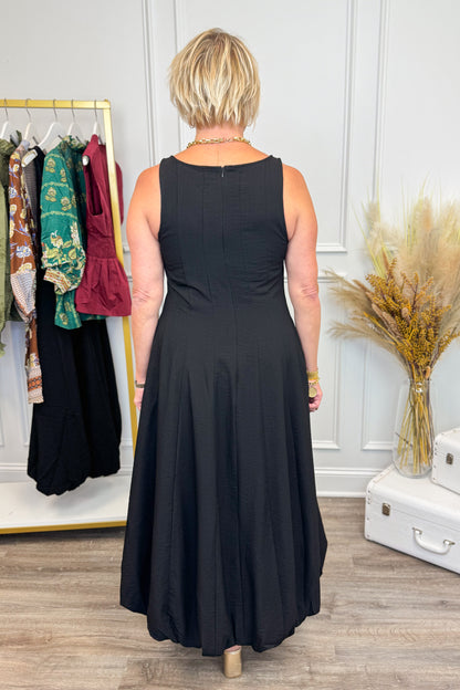 Back view of Woman wearing Black Bubble Hem Midi Dress with clothes in the background.