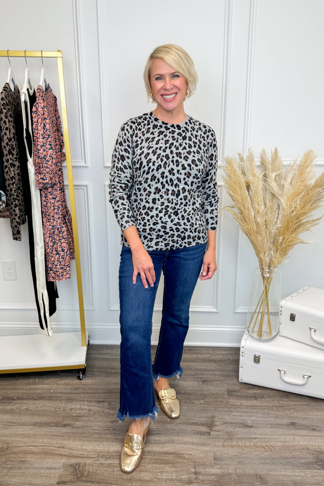 Front view of woman wearing Grey Leopard Crewneck Sweater with jeans against with decor in the background.