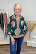 Woman wearing Hunter Green Printed & Textured Puff Sleeve Top and jeans with clothes in background.