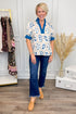 Woman wearing a floral blouse and blue jeans standing in a room with a rack of clothes and decorative items.