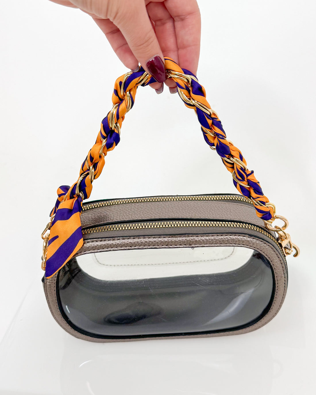 Handbag with a purple and yellow handle held by a hand on a white background