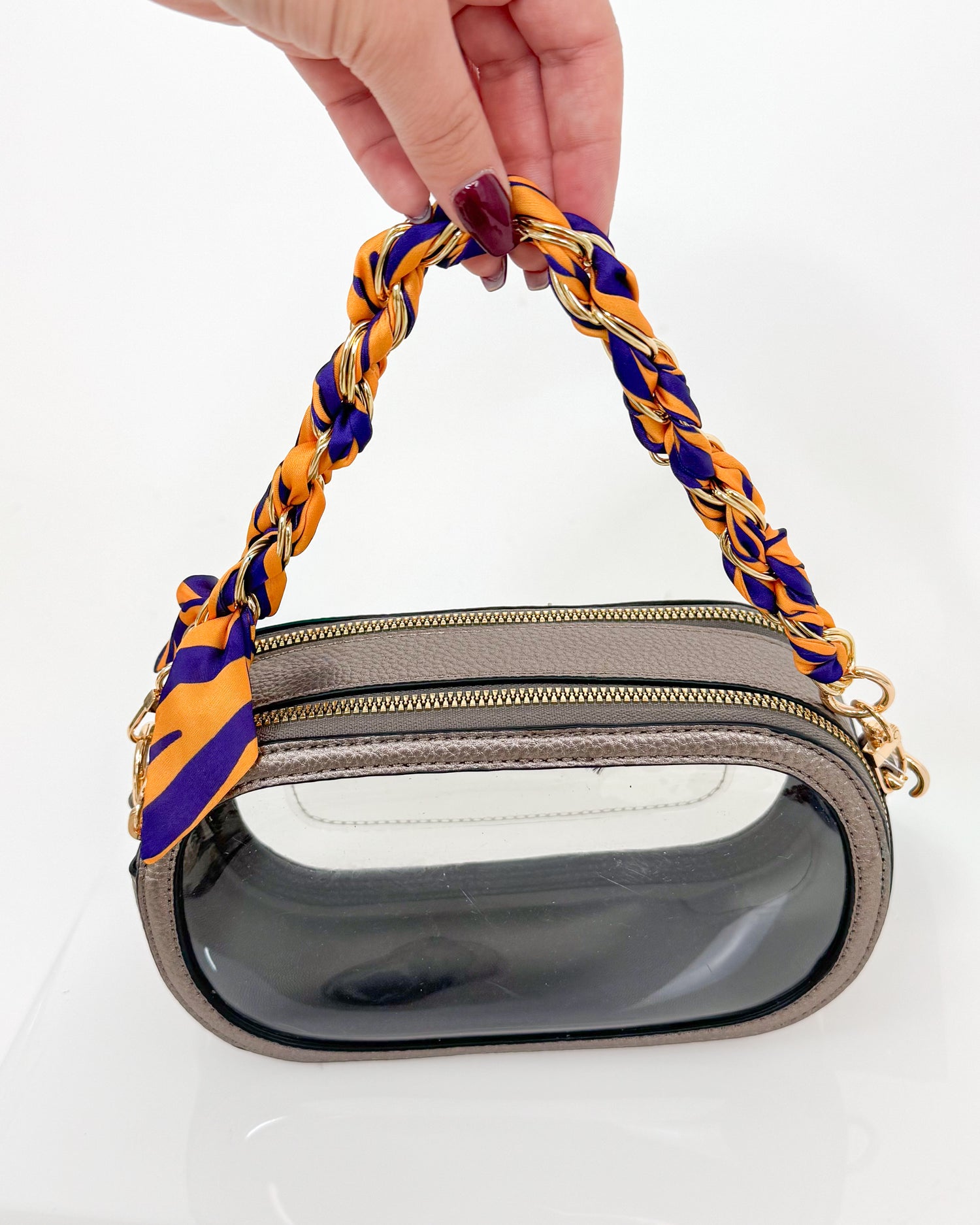 Handbag with a purple and yellow handle held by a hand on a white background