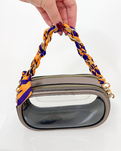 Handbag with a purple and yellow handle held by a hand on a white background