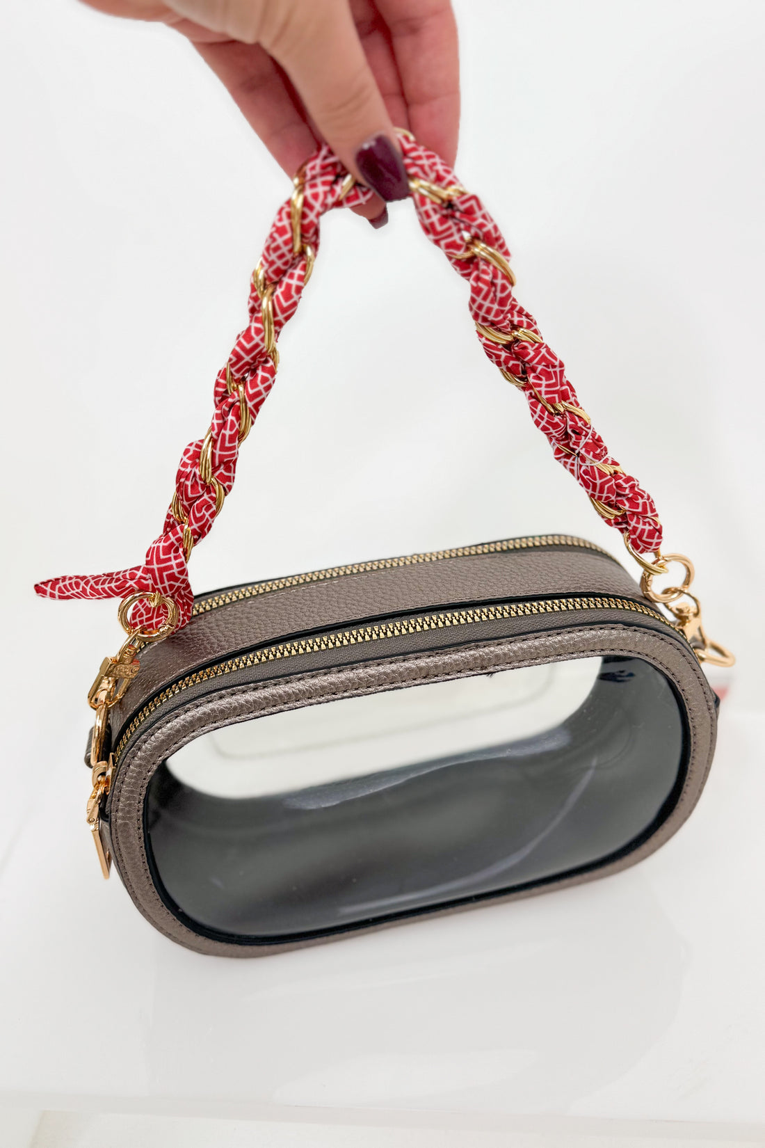 Handbag with a red floral handle held by a hand on a white background
