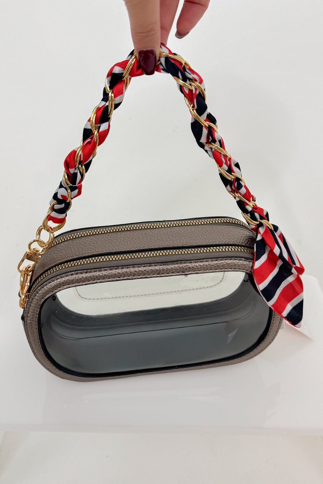 Handbag with a red, black, and white handle held by a hand on a white background