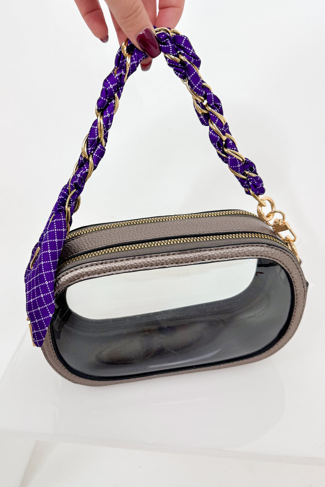 Handbag with a purple and gold handle held by a hand on a white background