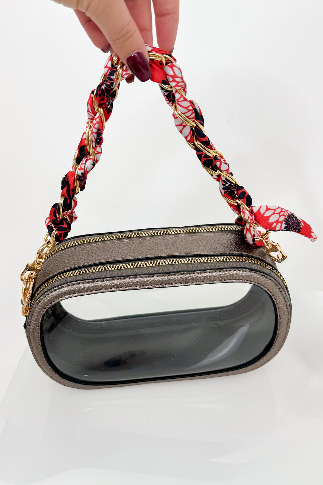 Handbag with a red, black, and white floral handle held by a hand on a white background