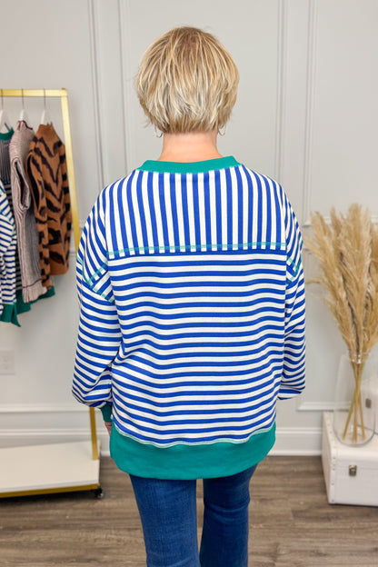 Person wearing a blue and white striped shirt with green trim in a clothing store.