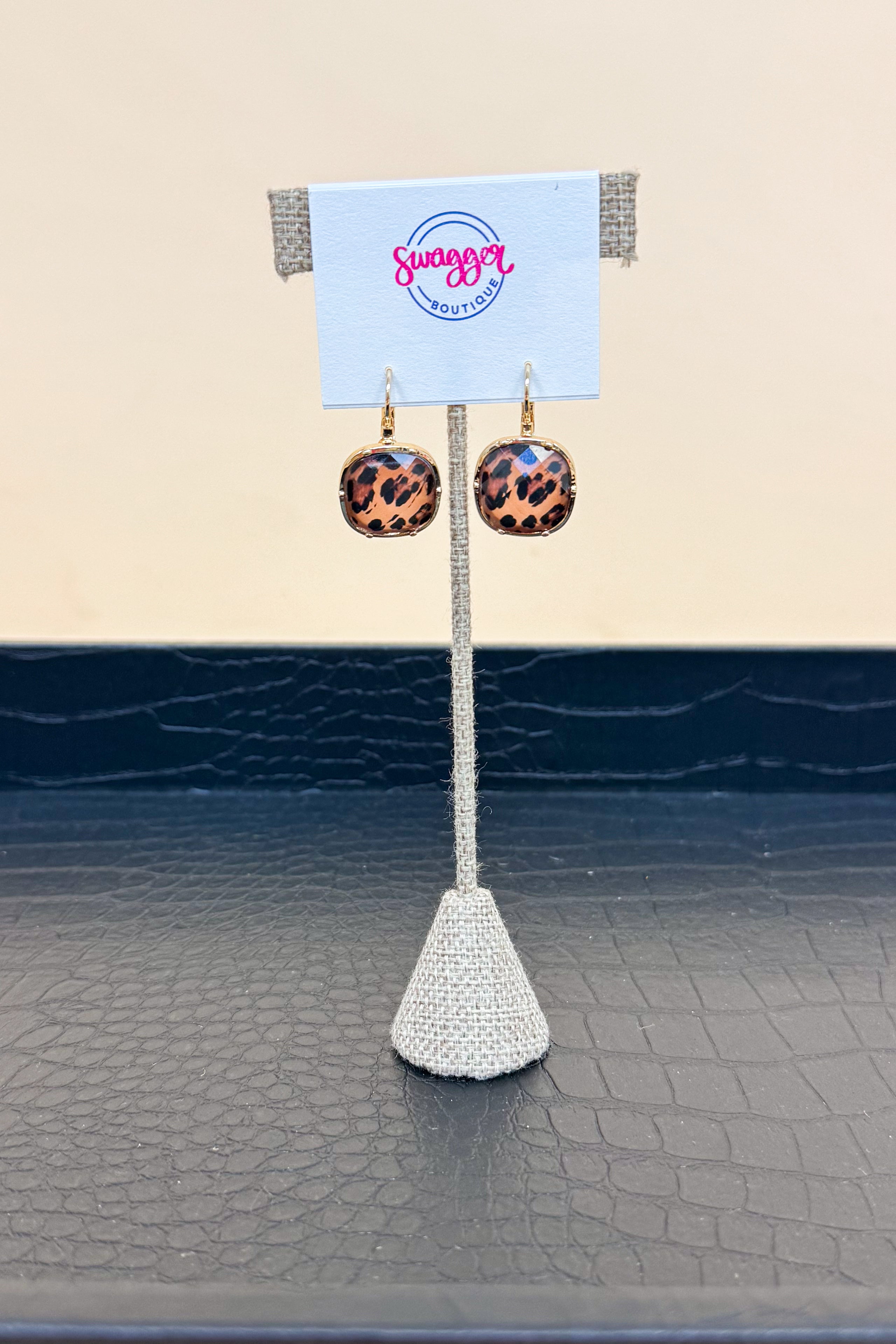 Pair of leopard print earrings on a white stand with a beige background