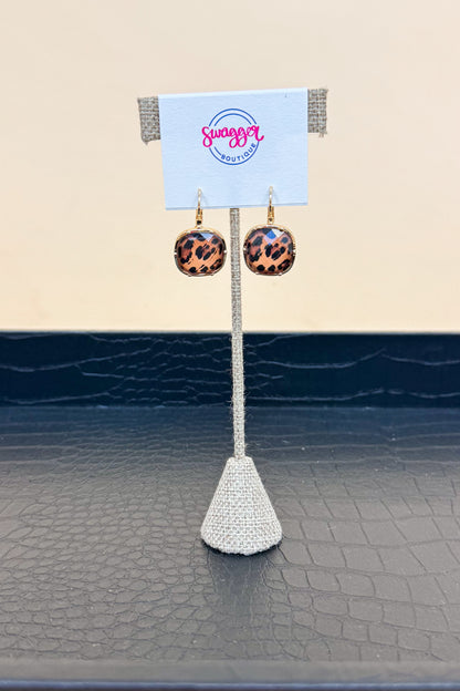 Pair of leopard print earrings on a white stand with a beige background