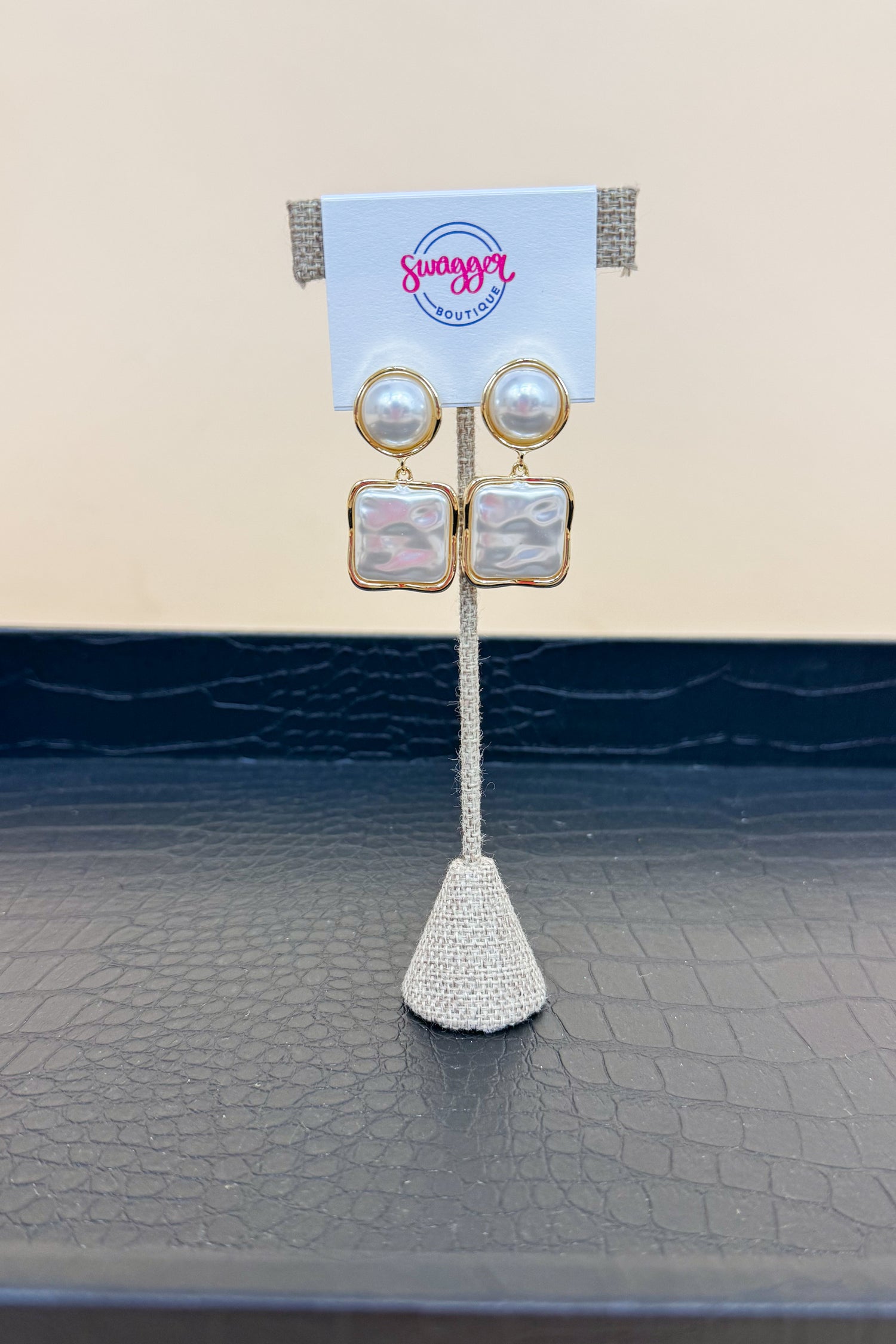 Pair of earrings on a stand with a branded card against a textured surface