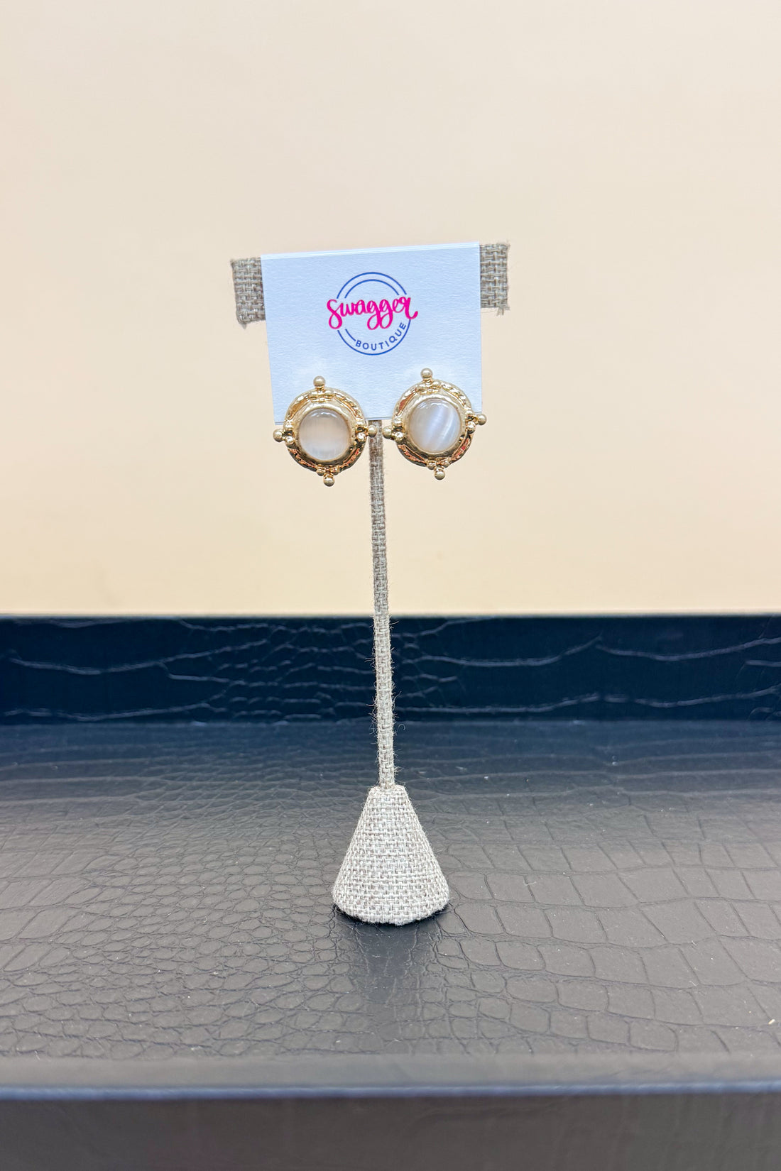 Pair of earrings on a stand with a branded card against a beige background
