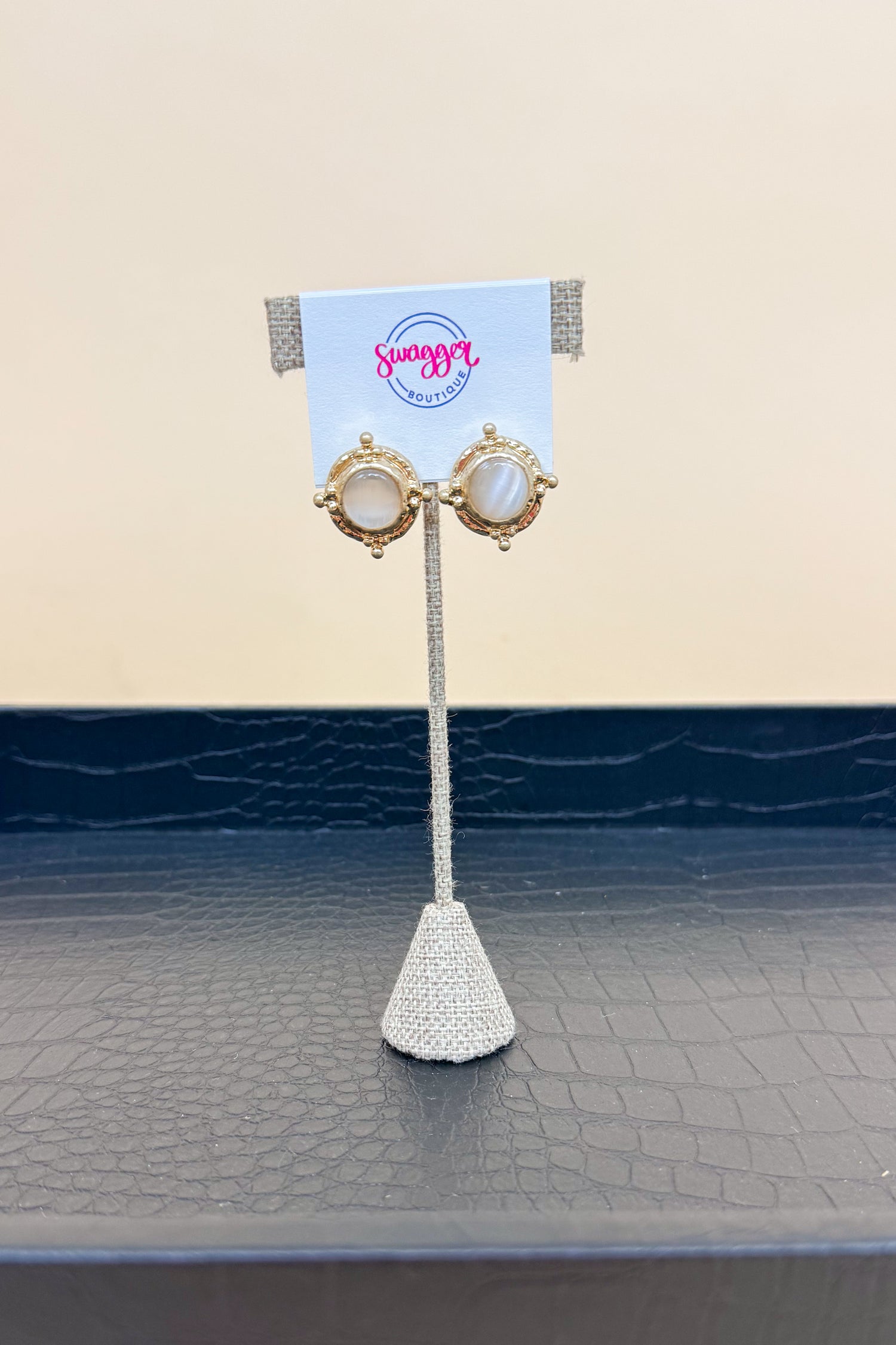 Pair of earrings on a stand with a branded card against a beige background