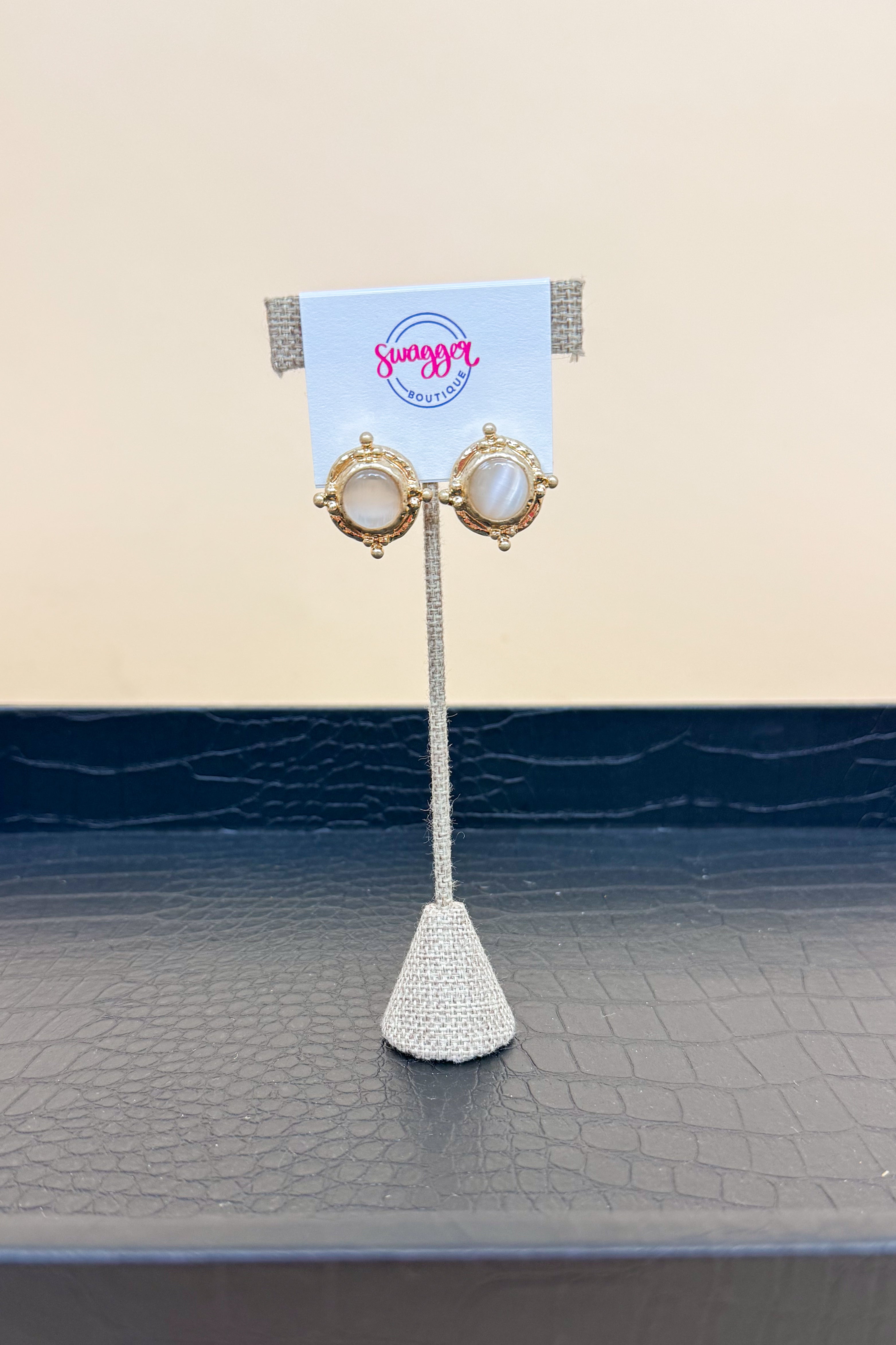 Pair of earrings on a stand with a branded card against a beige background